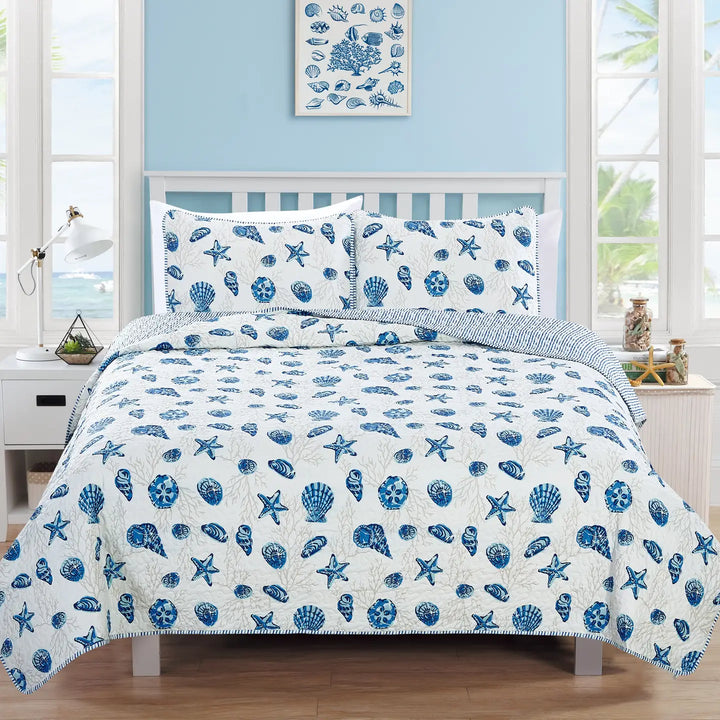Blue and white shell patterned bedding set on a bed in a bright room.