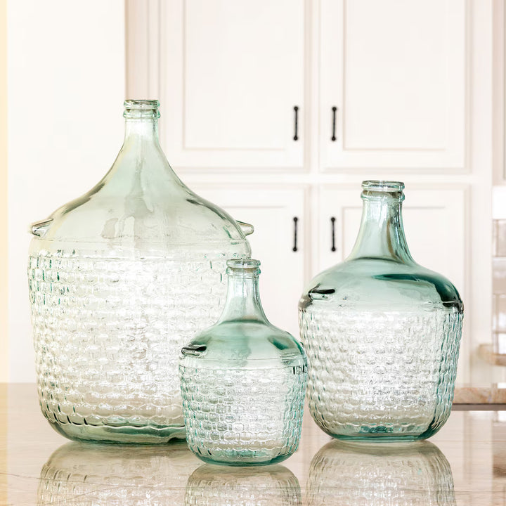 Three glass bottles with textured surfaces on a reflective surface.