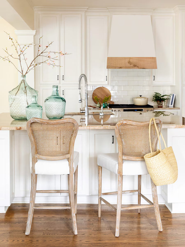 Modern kitchen with white cabinets, marble countertop, and rattan chairs with three glass vases on countertop