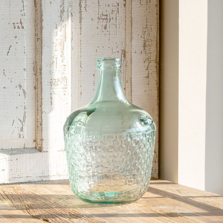 Clear glass bottle on a wooden surface with a textured wall background