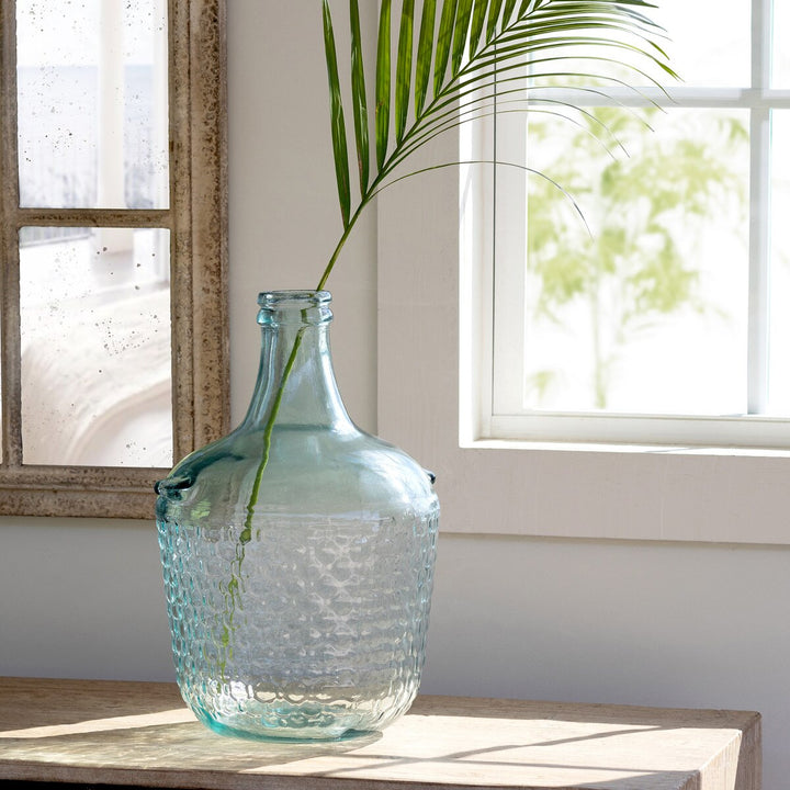Clear glass vase with textured surface on a wooden surface near a window.