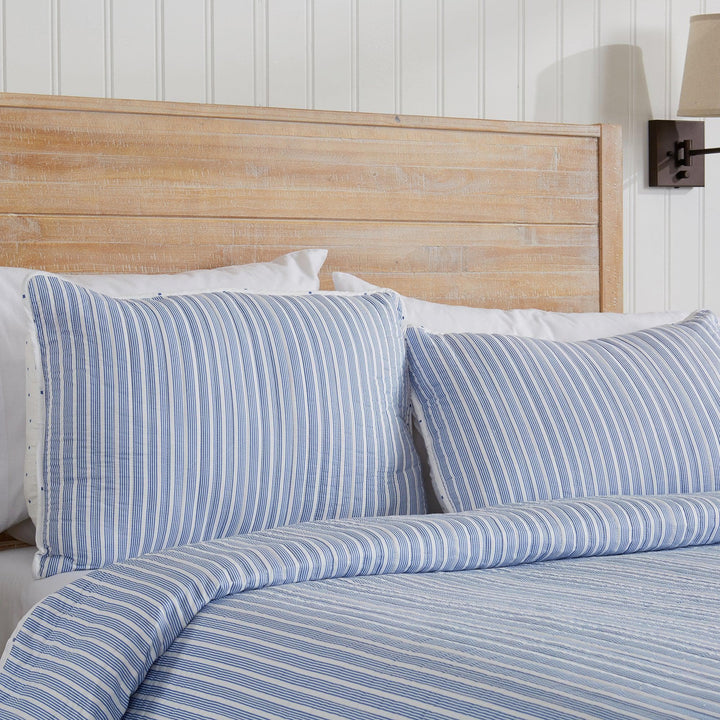 Bed with blue striped bedding and wooden headboard against a white paneled wall.
