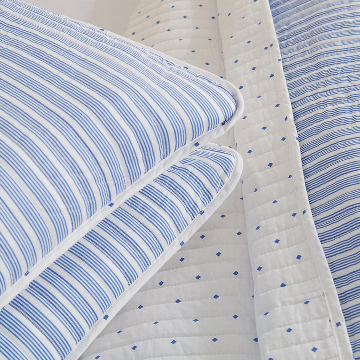 Blue and white striped bedding set with a quilt and pillows.