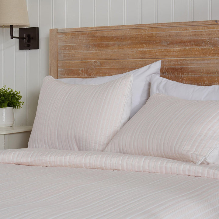 Bed with striped bedding and wooden headboard against a white paneled wall.