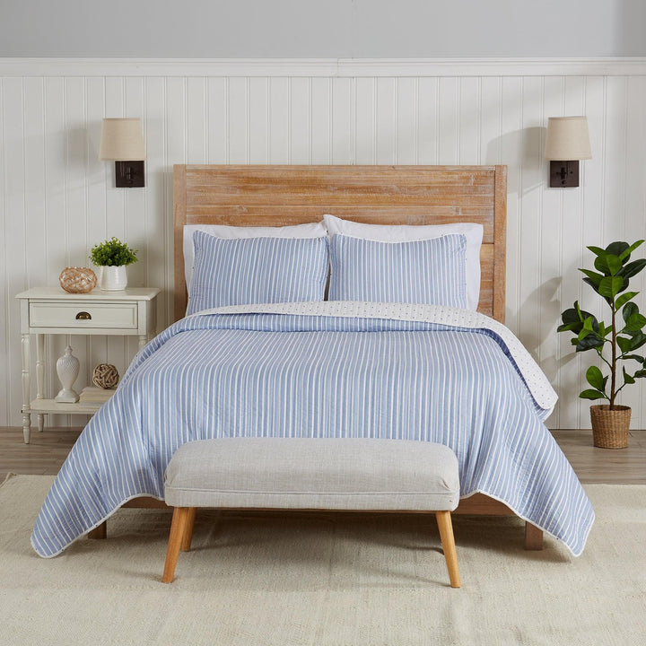 Bedroom with a bed covered in blue striped bedding, wooden headboard, and gray ottoman.