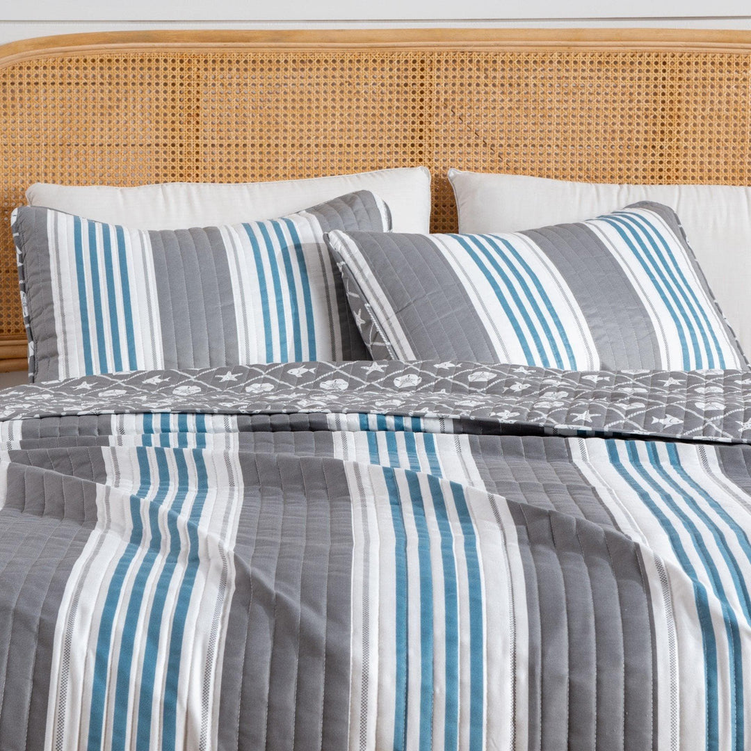 Striped bedding with blue and gray patterns on a bed with a wicker headboard.