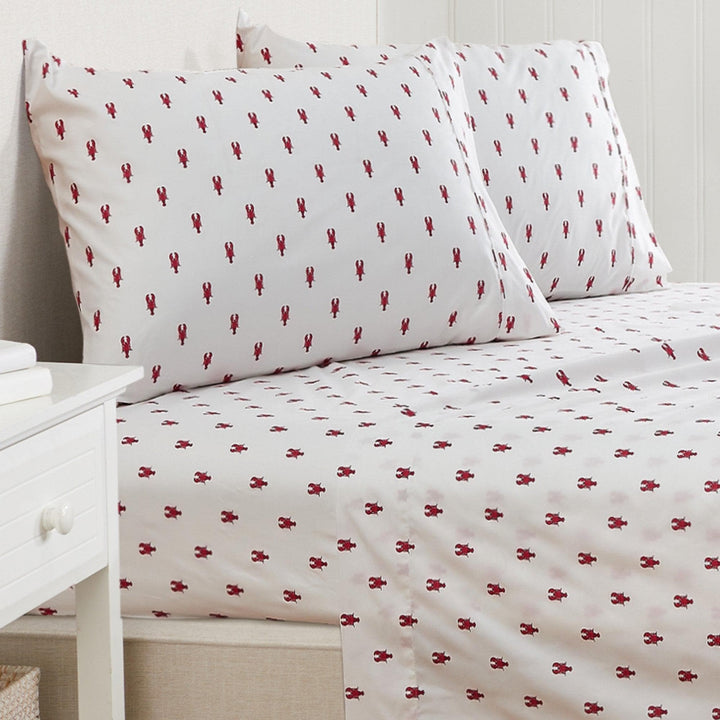 White sheets and pillowcase set with red lobster pattern on bed.