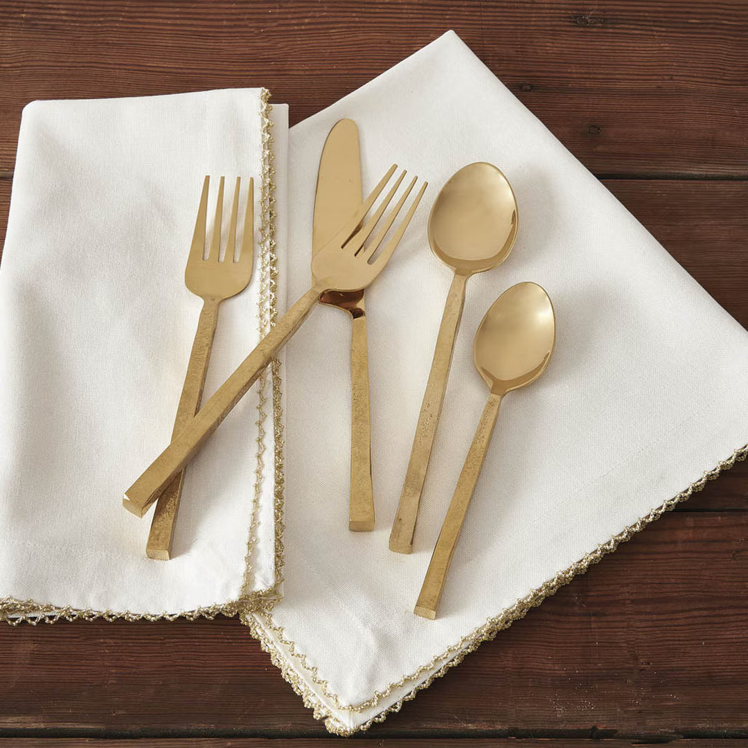 Avis Gold square handled flatware set on white and gold napkins with a wood background