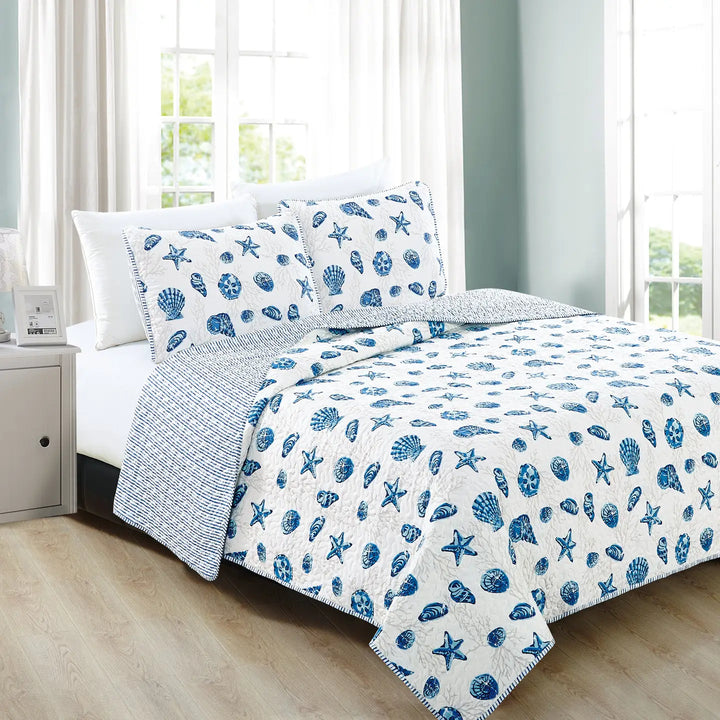 Bed with blue and white shell patterned bedding in a bright room.