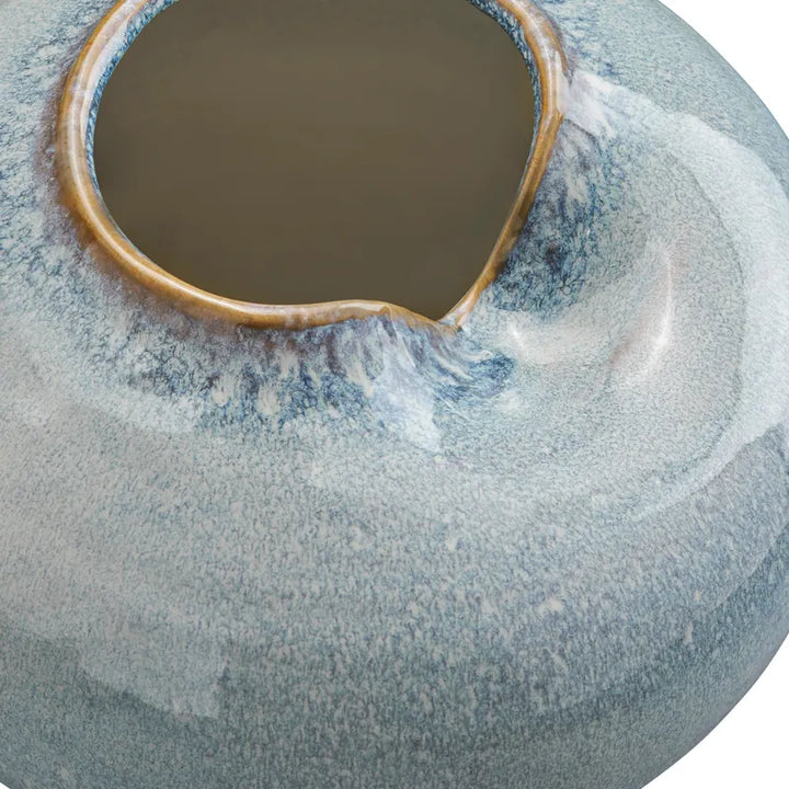 Close-up of a ceramic vase with a rounded, bulbous shape and a wide flared opening. The glaze is predominantly a mottled light blue and white with a warm tan-brown rim around the opening.