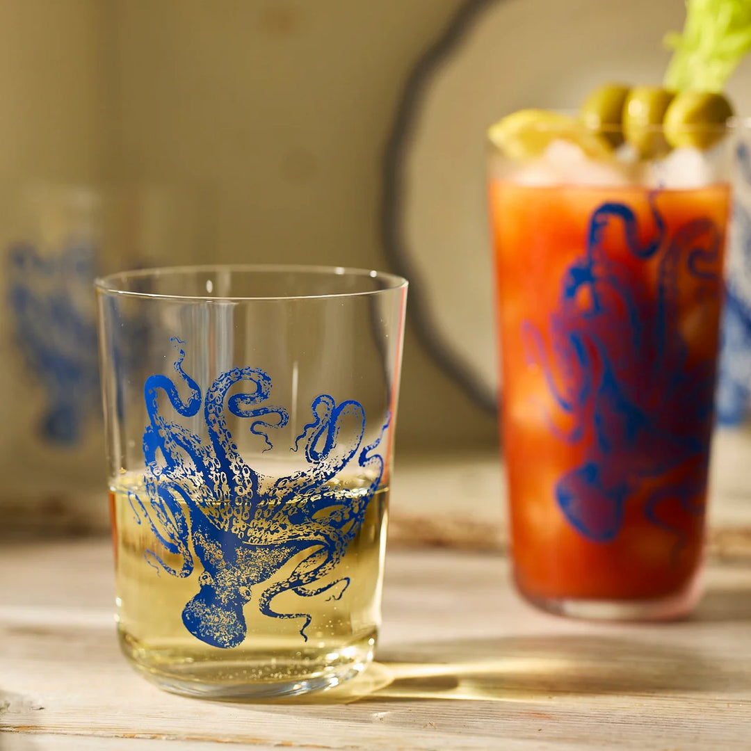 Clear glass with blue octopus design next to a Bloody Mary cocktail on a wooden surface.