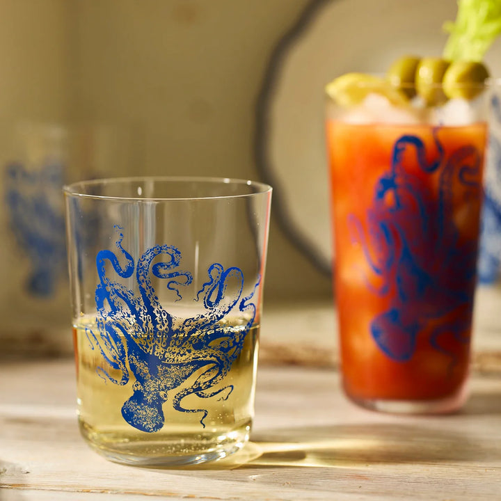 Clear glass with blue octopus design next to a Bloody Mary cocktail on a wooden surface.
