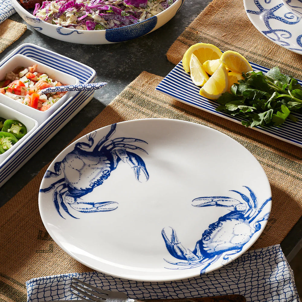 White plate with blue crab design on a table with food and tableware.
