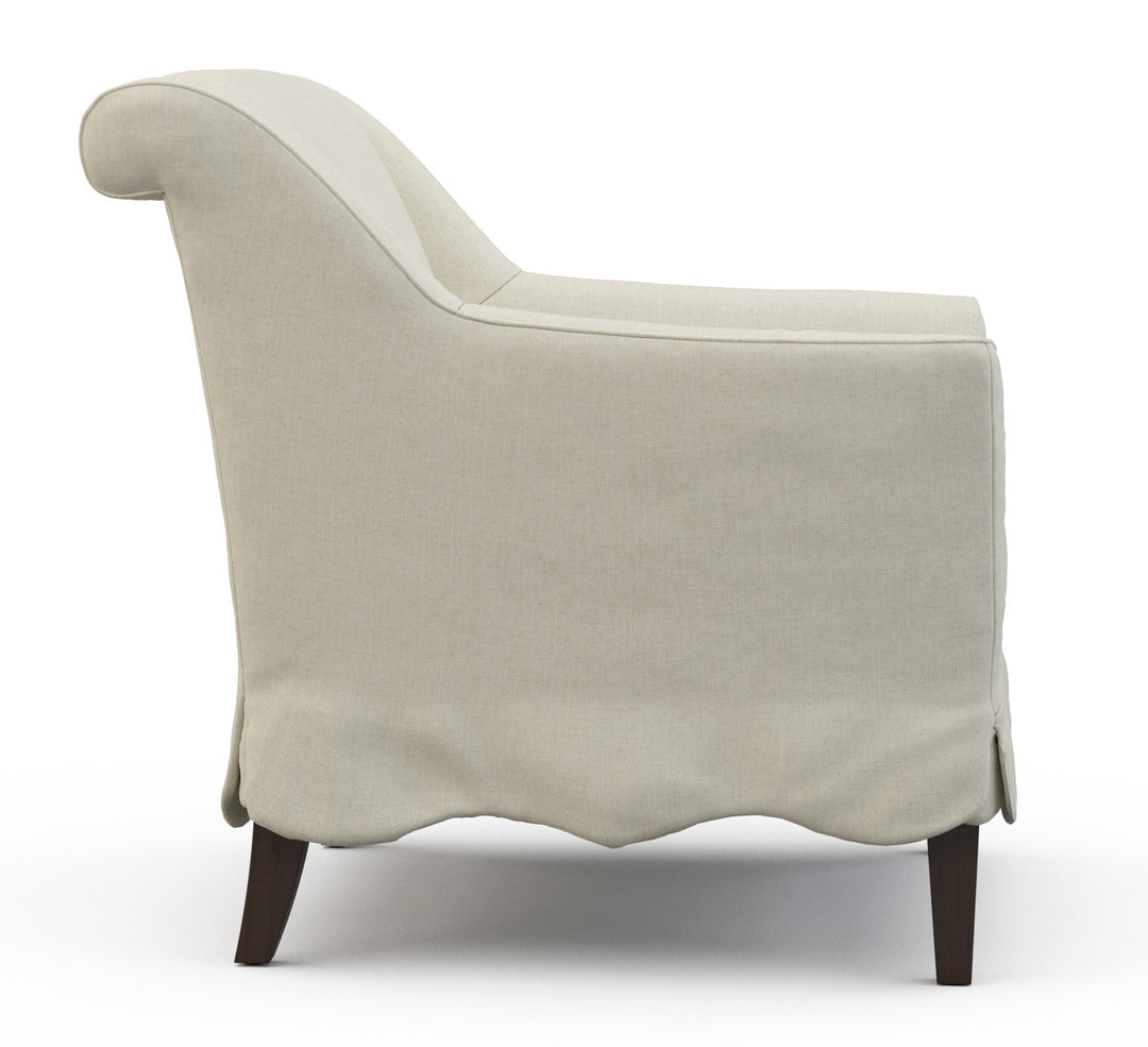 Beige armchair with rolled back edge and scalloped chair skirt and wood legs. Coastal Compass