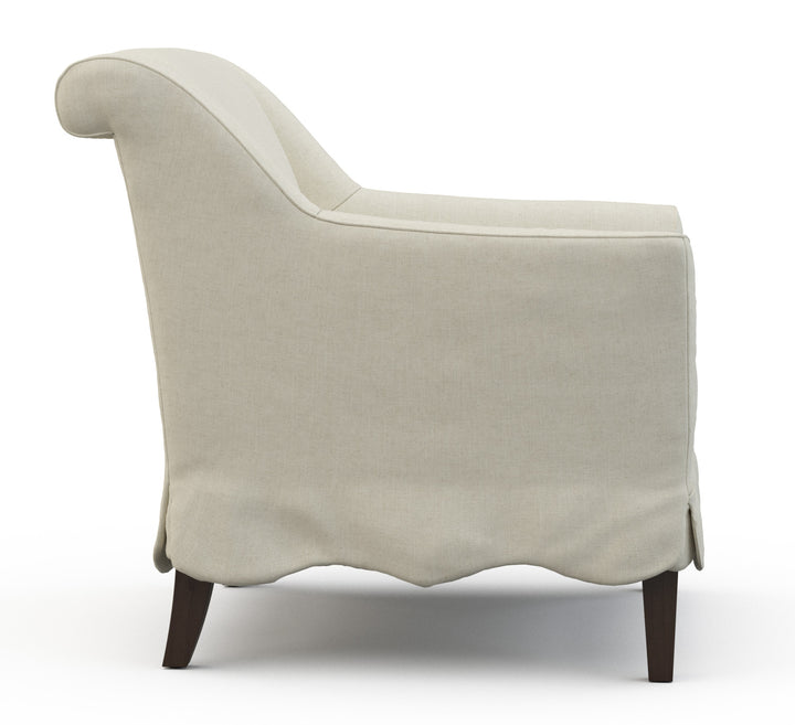 Beige armchair with rolled back edge and scalloped chair skirt and wood legs. Coastal Compass