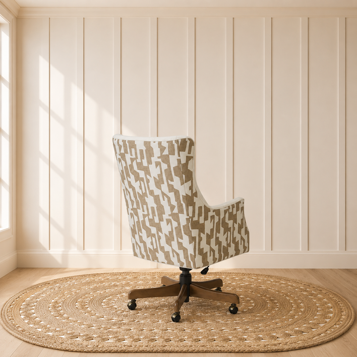 A wingback office chair with a beige and white geometric patterned fabric upholstery, mounted on a dark wood five-star swivel base with casters, set on a round woven jute rug in a room with cream paneled walls and light wood floors.