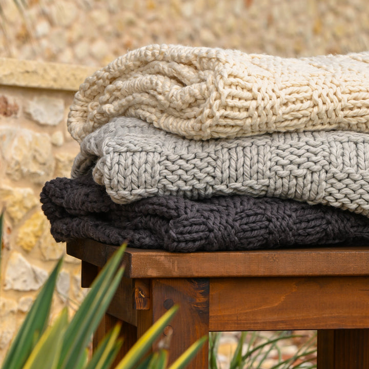 Stack of knitted blankets in beige, gray, and black on a wooden surface- Coastal Compass Home Decor