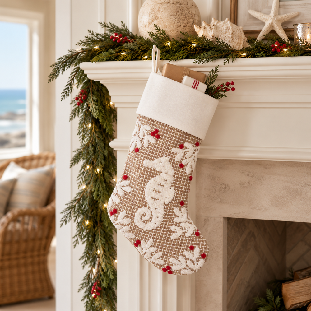 Coastal seahorse Christmas stocking with a white cuff, textured beige fabric, and red berry accents hanging from a festive fireplace mantel decorated with greenery, seashells, and warm holiday lights.