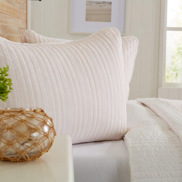 Neatly made bed with textured pillows and a decorative vase in a softly lit room.