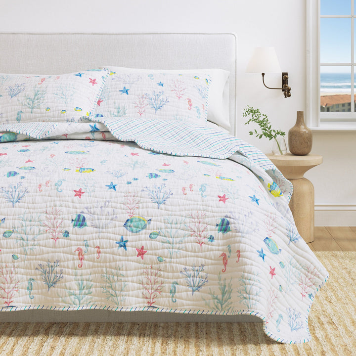 Bed with a colorful quilt featuring sea-themed patterns in a bright bedroom.