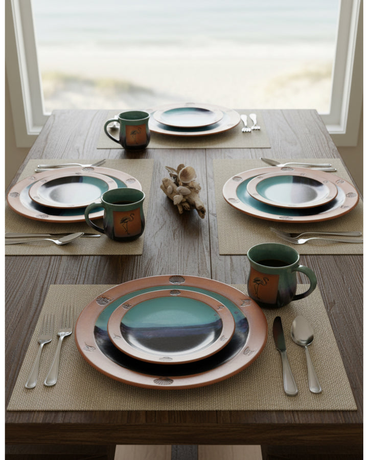 Dining table set with ceramic plates, mugs, and cutlery on a wooden surface.