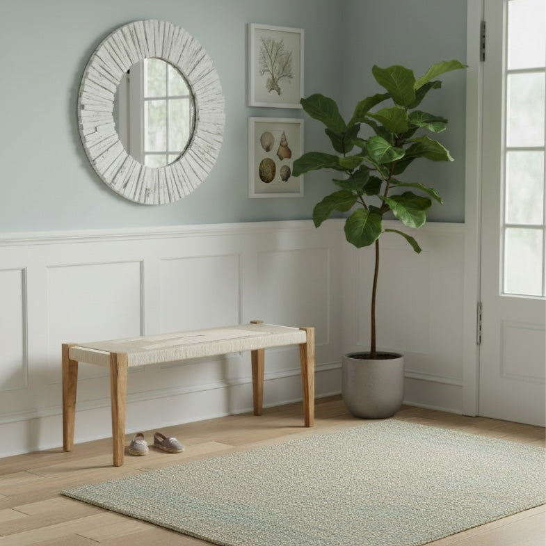 Natural wood and rope woven bench styled in a coastal entryway with soft green walls, round textured mirror, and neutral decor accents