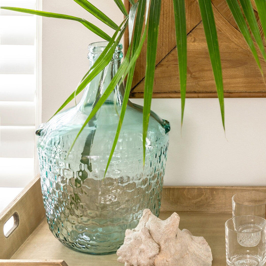 Decorative glass vase with textured surface on a wooden surface, surrounded by green leaves.