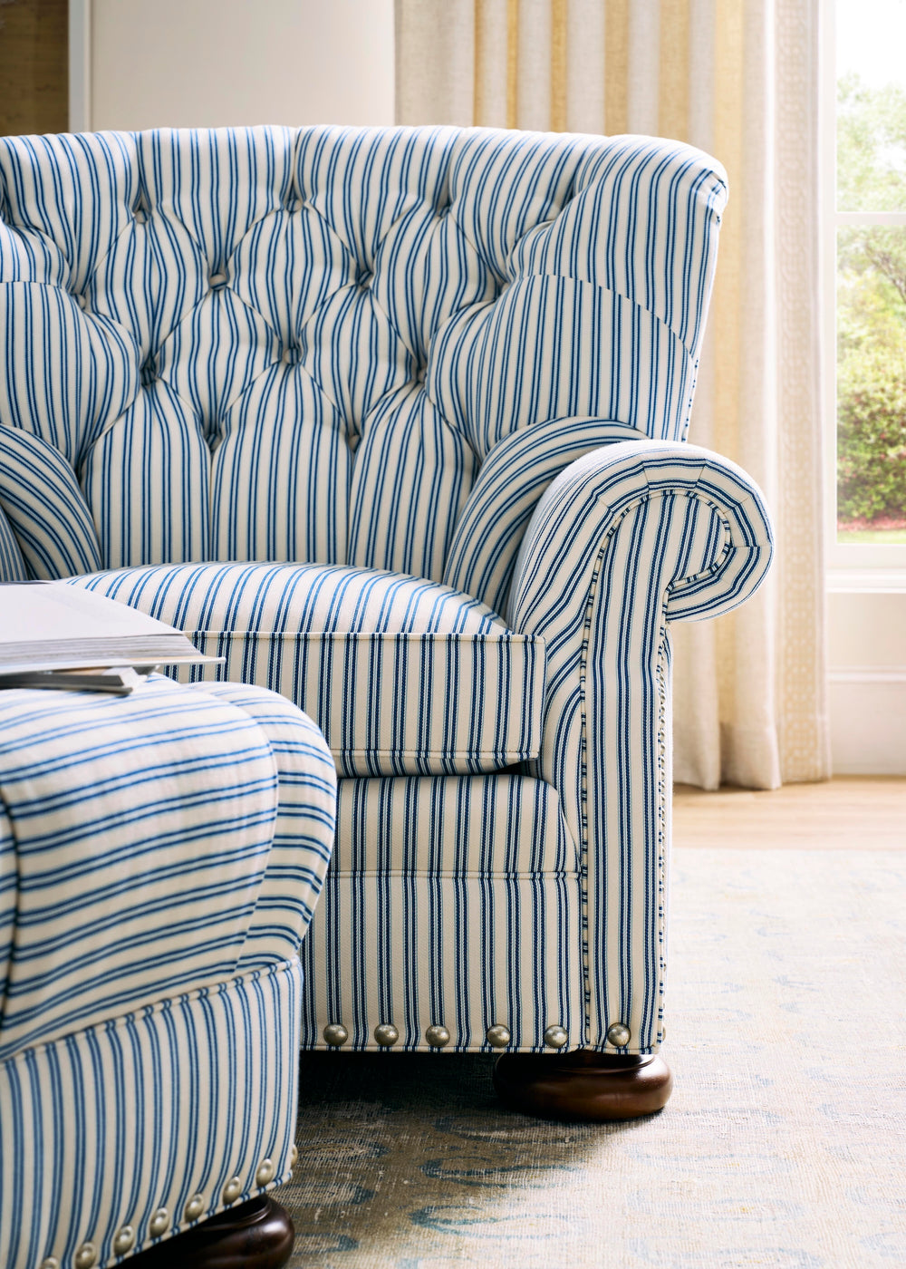 Blue and white striped armchair with tufted backrest in a room with curtains. Coastal Compass
