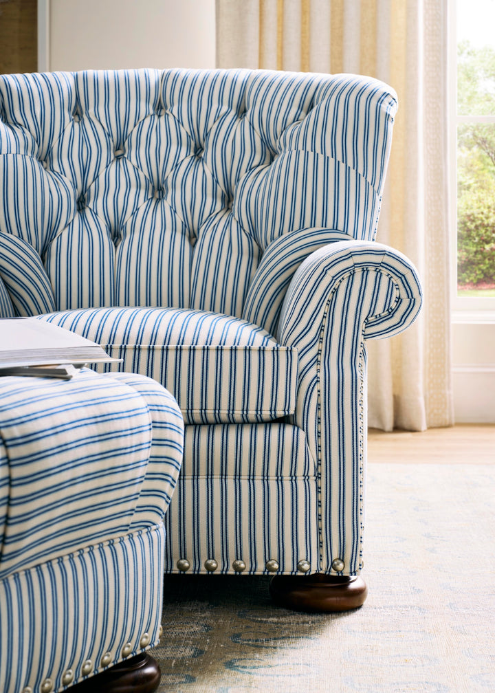 Blue and white striped armchair with tufted backrest in a room with curtains. Coastal Compass