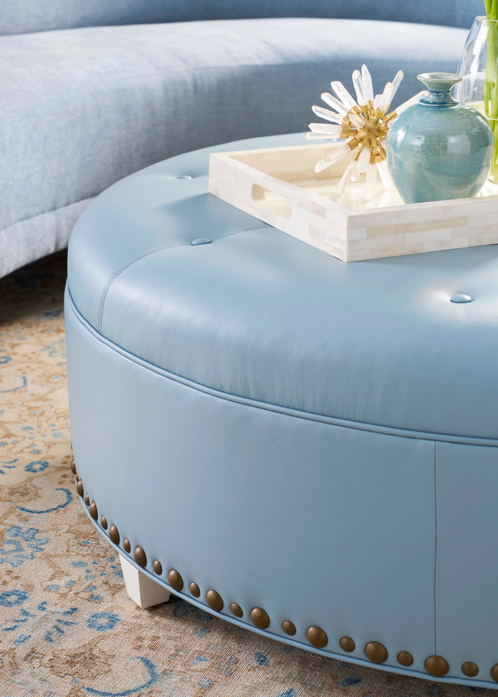 Round light blue ottoman with decorative items on a patterned rug. Coastal Compass Home Decor