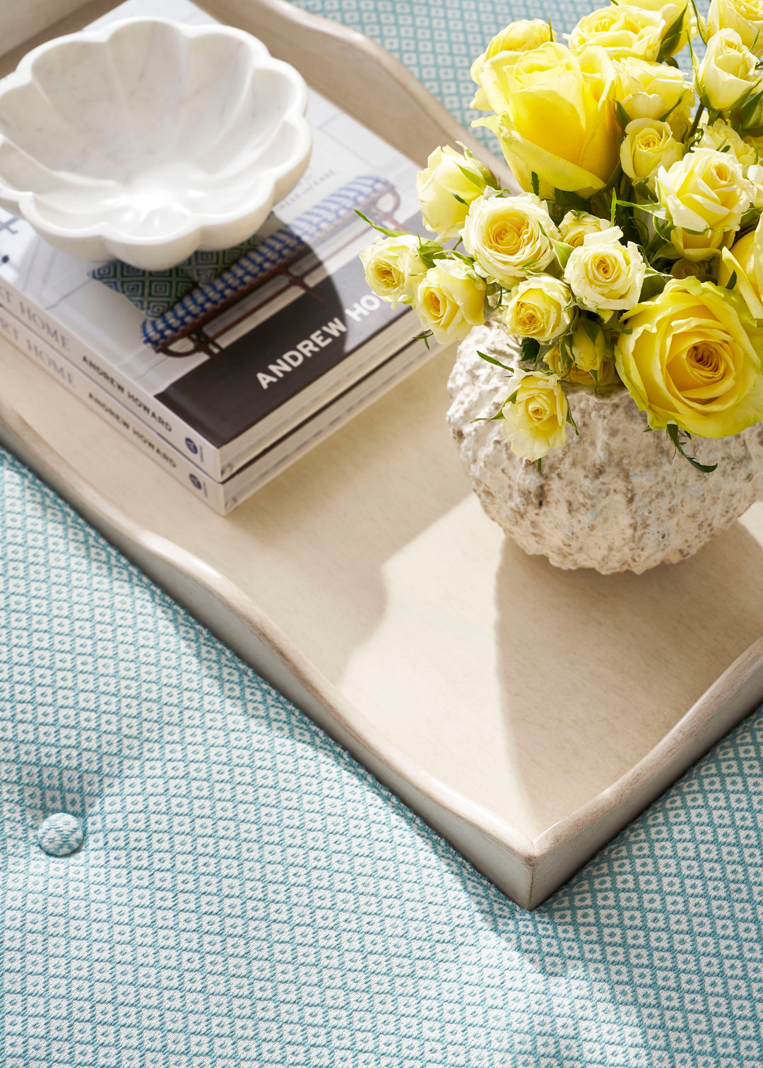 Decorative tray with books and a vase of yellow flowers on a textured surface