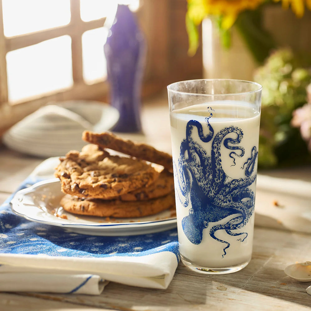 Glass of milk with blue octopus design next to cookies on a wooden table.