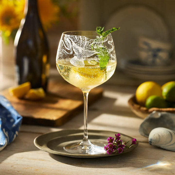 Cocktail in a decorative glass with garnishes on a wooden table. Coastal Compass Home Decor