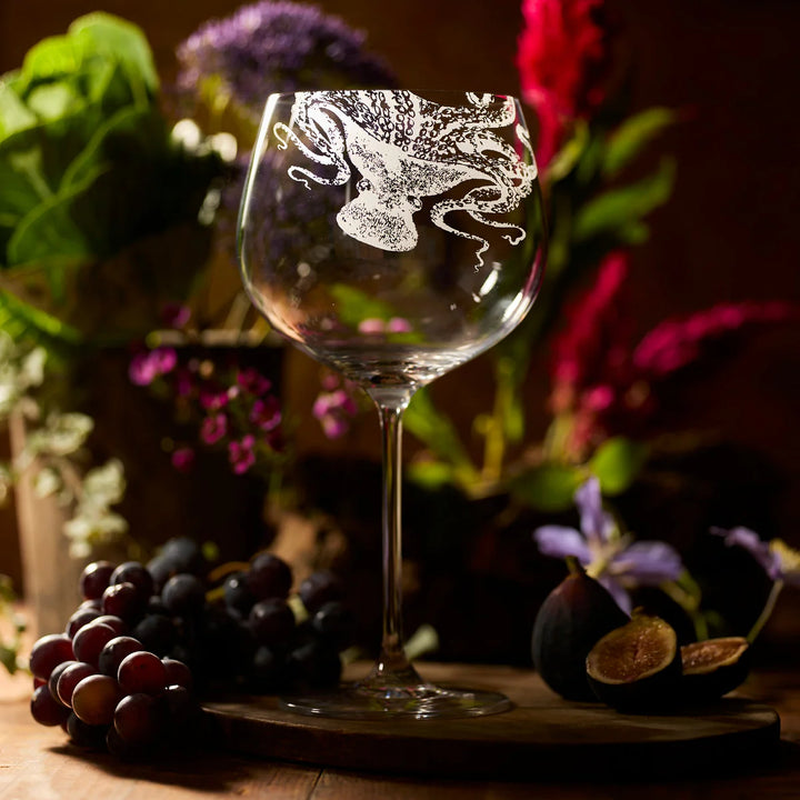 Decorative wine glass with floral engraving on a wooden surface with grapes and figs. Coastal Compass Home Decor