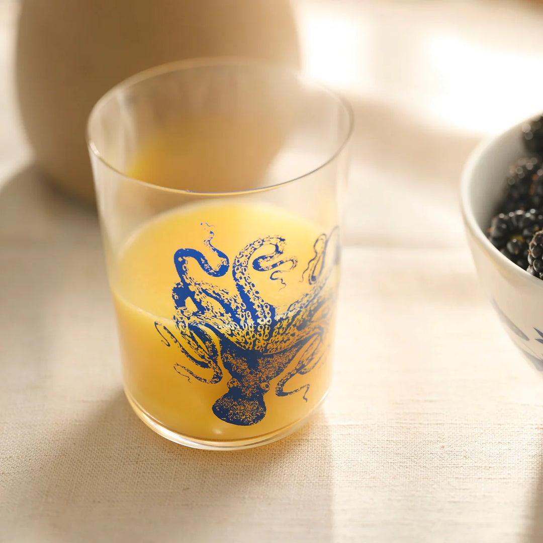 Glass with blue dragon design filled with a yellow liquid on a light surface.