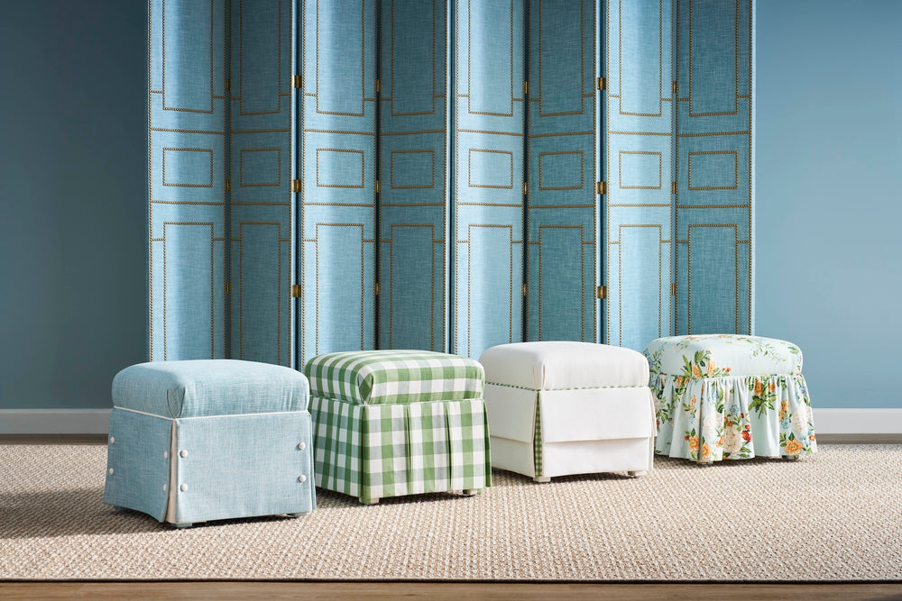 Four upholstered ottomans in different styles and colors against a blue paneled wall.
