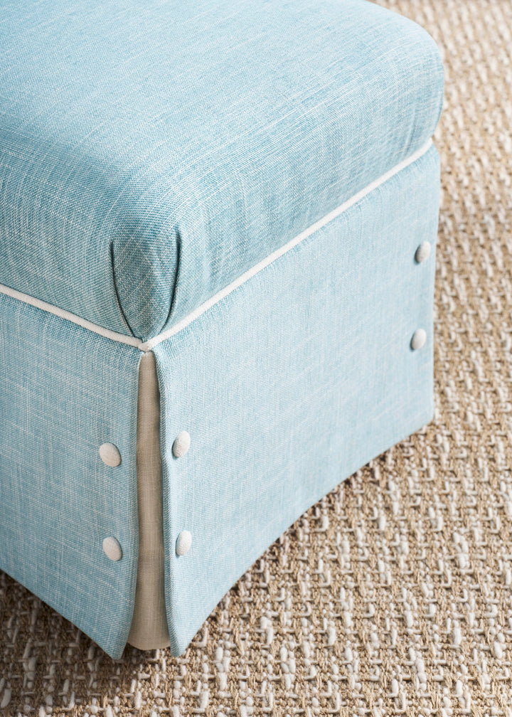 Light blue ottoman with white trim on a textured beige carpet