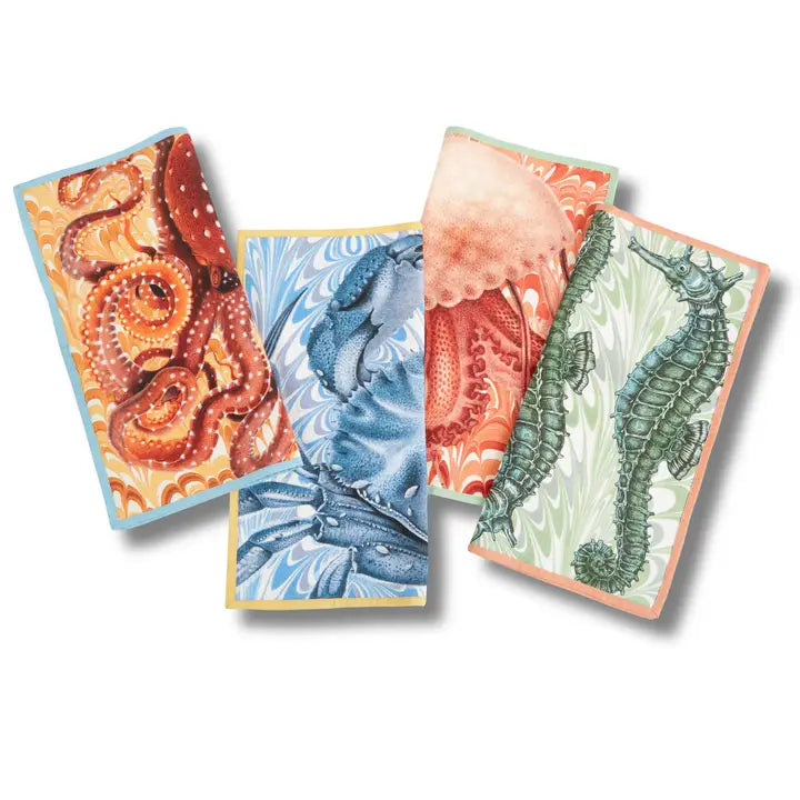 Set of four colorful coastal cotton dinner napkins featuring octopus, crab, jellyfish, and seahorse designs with marbled backgrounds and contrasting borders.