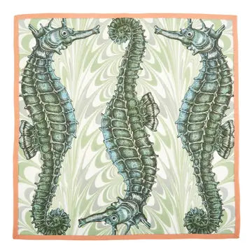 Coastal cotton napkin featuring detailed green seahorse illustrations on a marbled seafoam background with coral trim.
