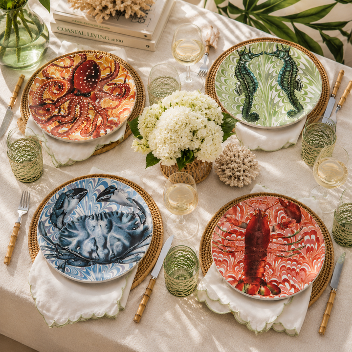 Coastal-inspired melamine dinner plate set styled together with colorful sea life artwork including crab, lobster, octopus, and seahorse designs.