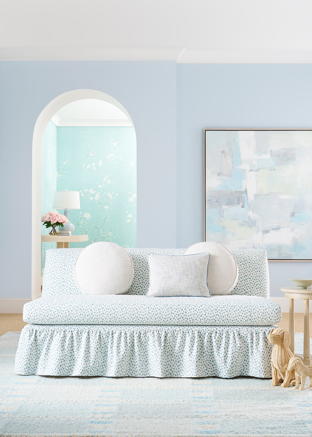 Light blue sofa with decorative pillows in a room with a light blue wall and a painting.