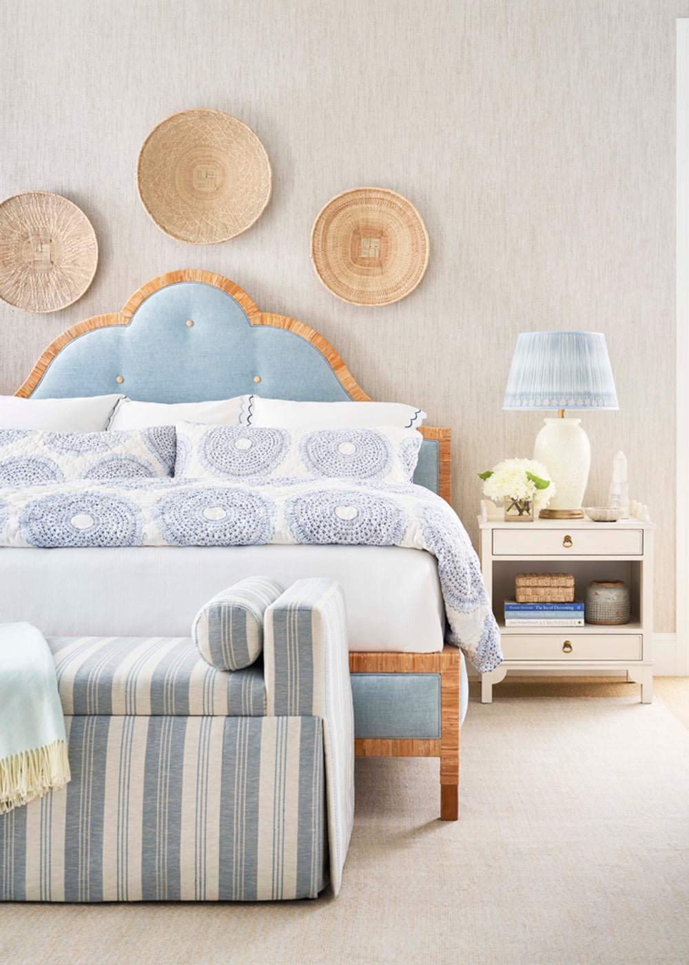 Neatly made bed with decorative pillows and striped footstool in a bedroom setting. Coastal Compass Home decor
