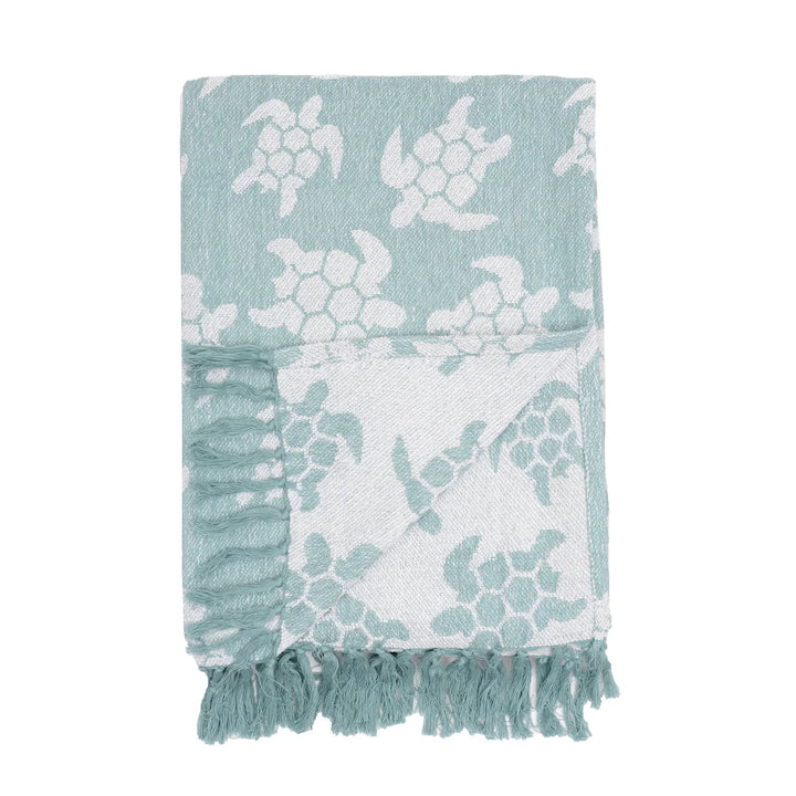 Teal and white throw blanket with turtle pattern and fringed edges on a white background