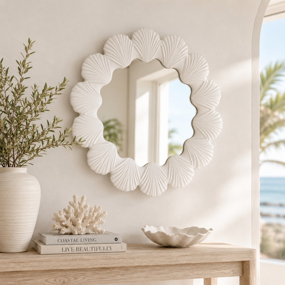Decorative shell-patterned mirror on a wall with a vase and books on a table.