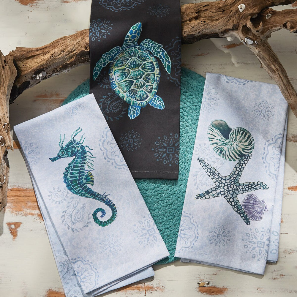 Set of three decorative towels with sea-themed designs on a wooden surface.