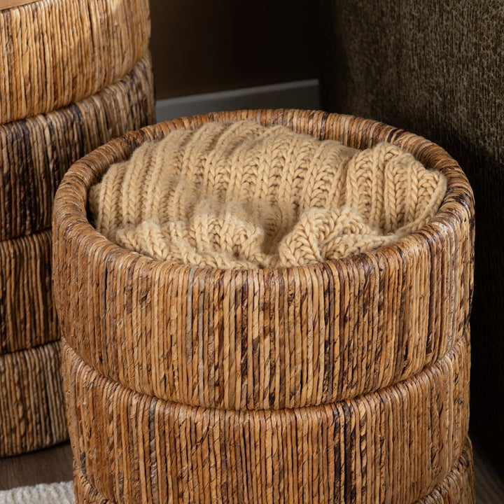 A round woven rattan storage with a thick, chunky knit beige cushion inside, shown in a close-up interior setting.