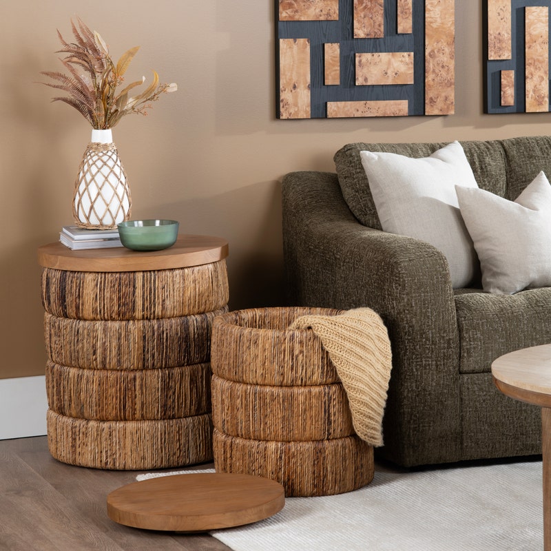 A styled living room corner featuring a round woven side table set with storage lids in a warm neutral setting.