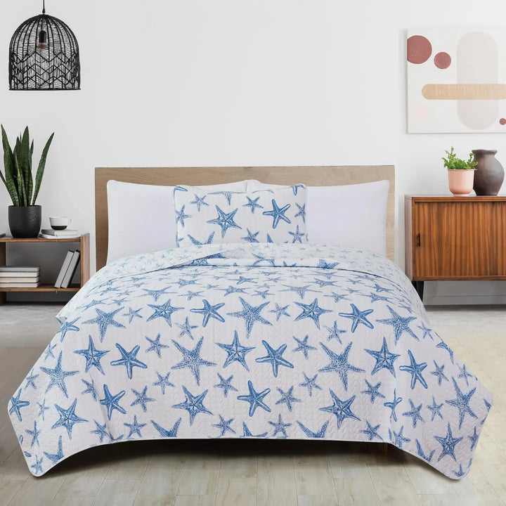Bed with blue starfish patterned quilt and pillows in a bedroom setting.