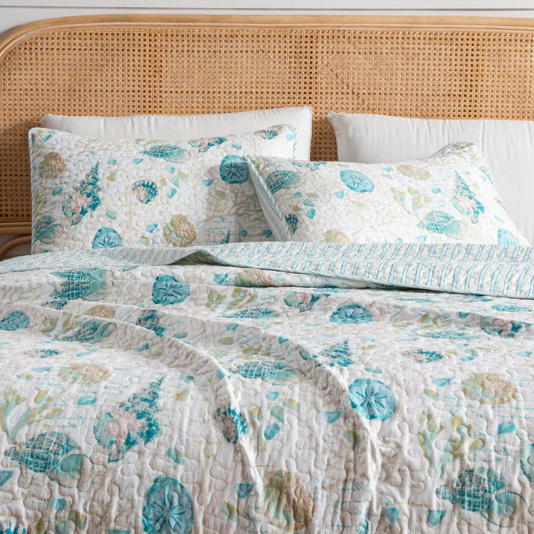 West Sands Quilt Set with matching pillow shams featuring blue and green seashell motifs on a cane wood bed
