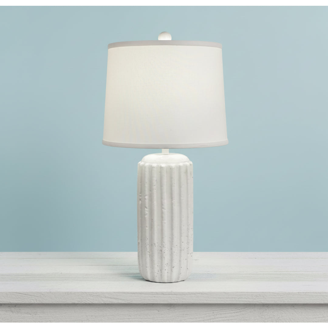White textured table lamp with a white shade on a light gray surface against a light blue background
